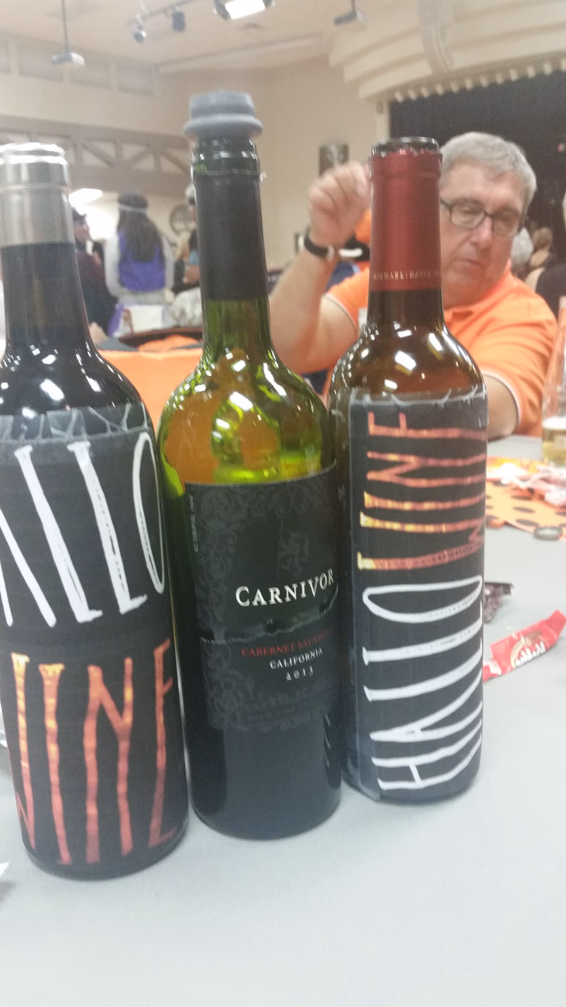 Wine bottles on a table with people dining indoors.