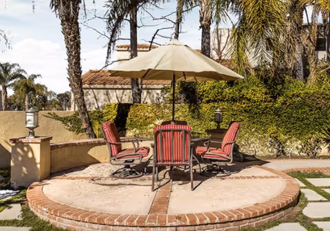 Round brick patio with red chairs and umbrella in a landscaped outdoor area.