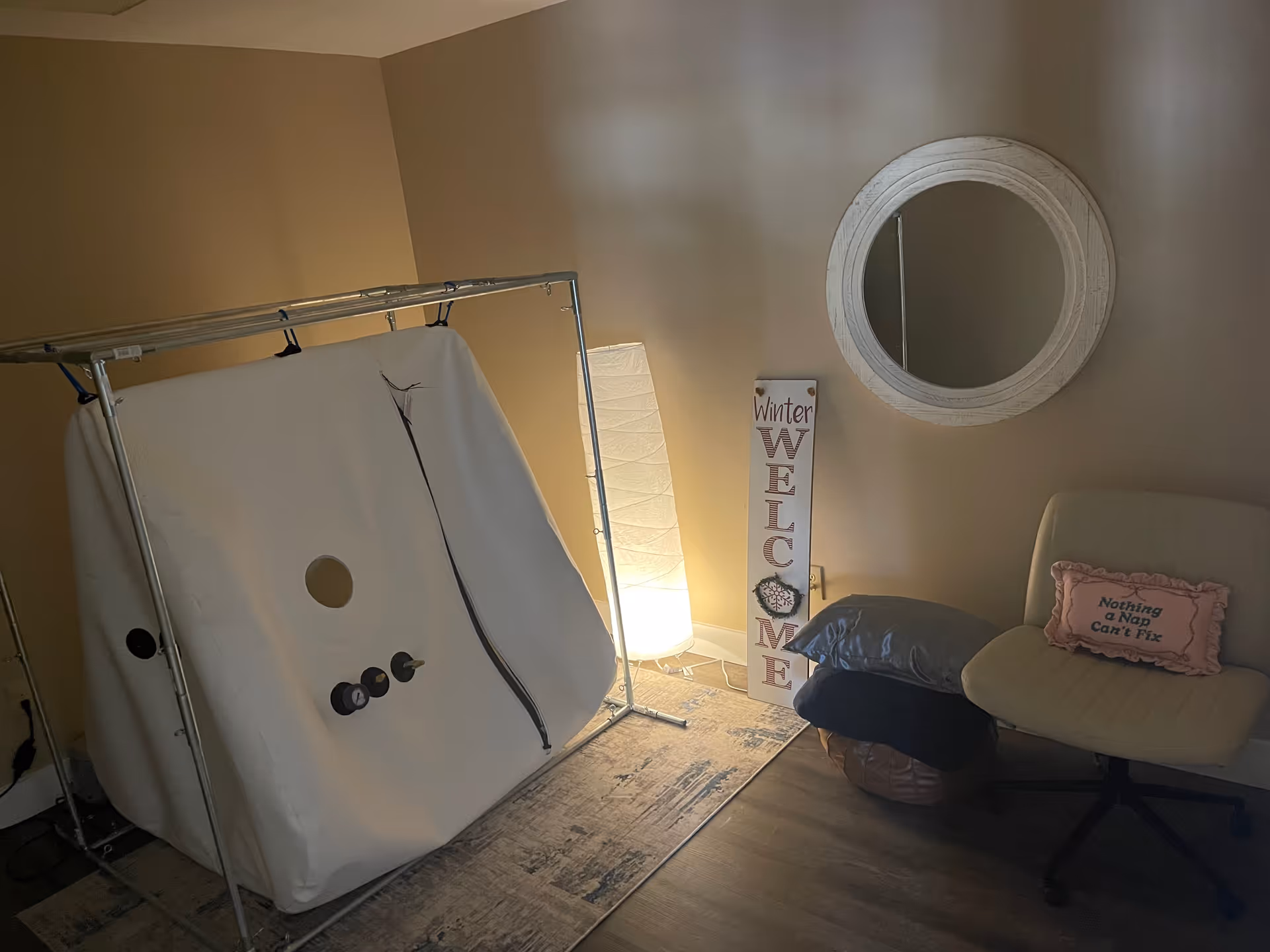 Small cozy interior room with a white portable tent, chair, round mirror, and welcome sign.