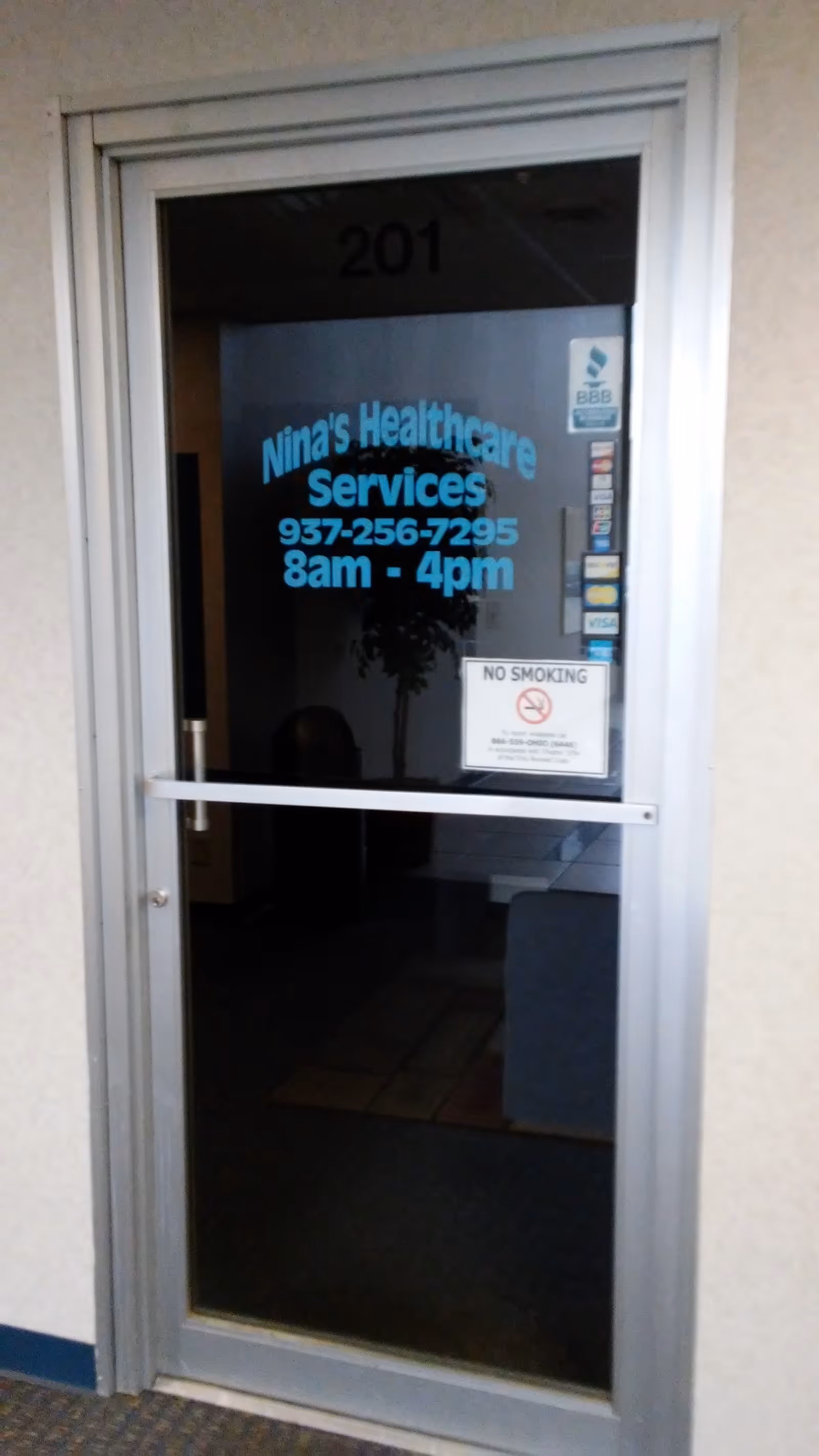 Glass door displays Nina's Healthcare Services sign with hours 8am-4pm and no smoking notice.