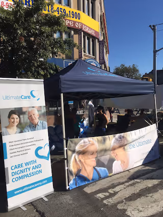Outdoor tent with UltimateCare banners and staff outside a building.