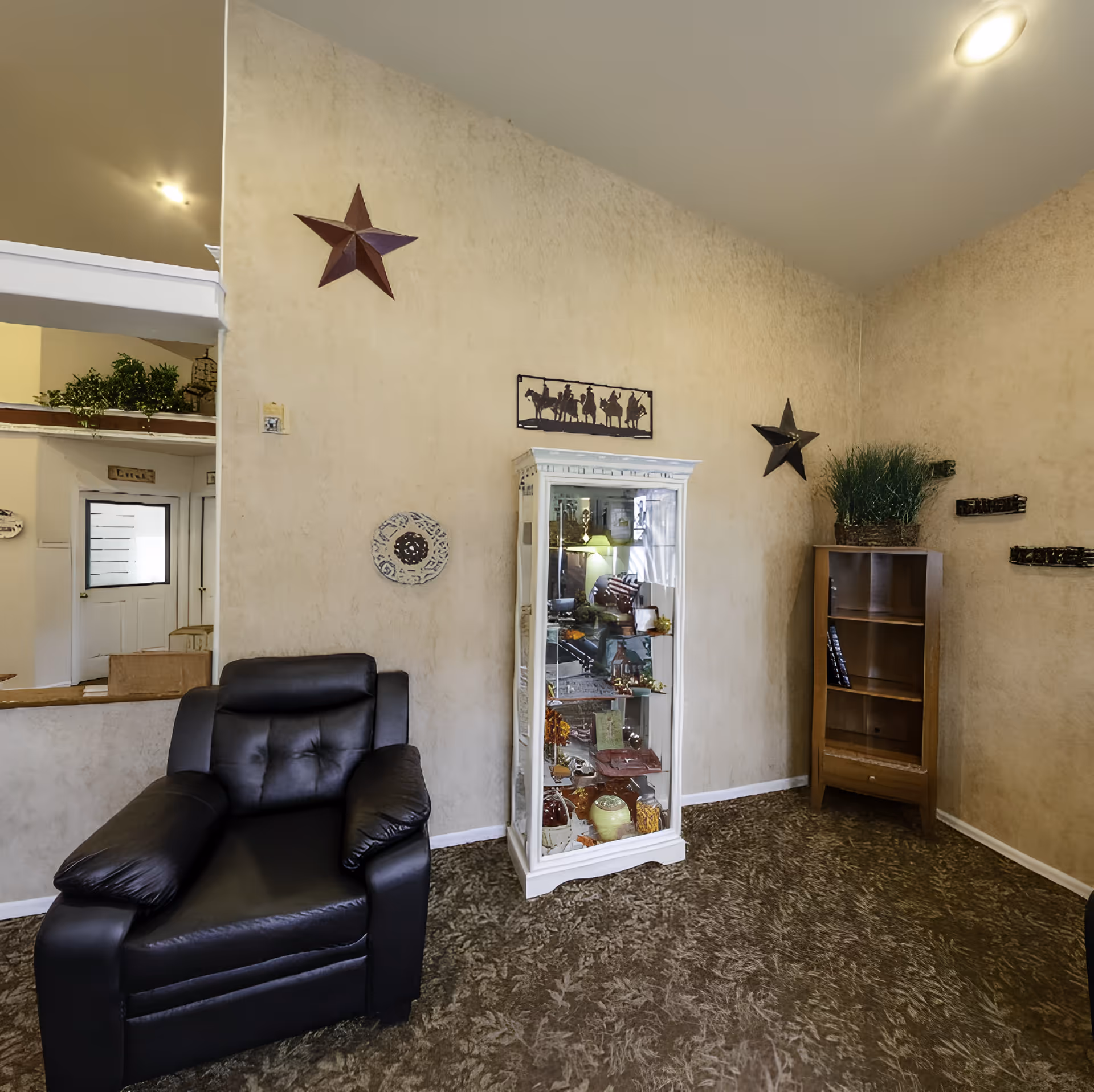 Cozy interior lounge with a black leather armchair, glass display cabinet, wooden shelving, and wall decorations.