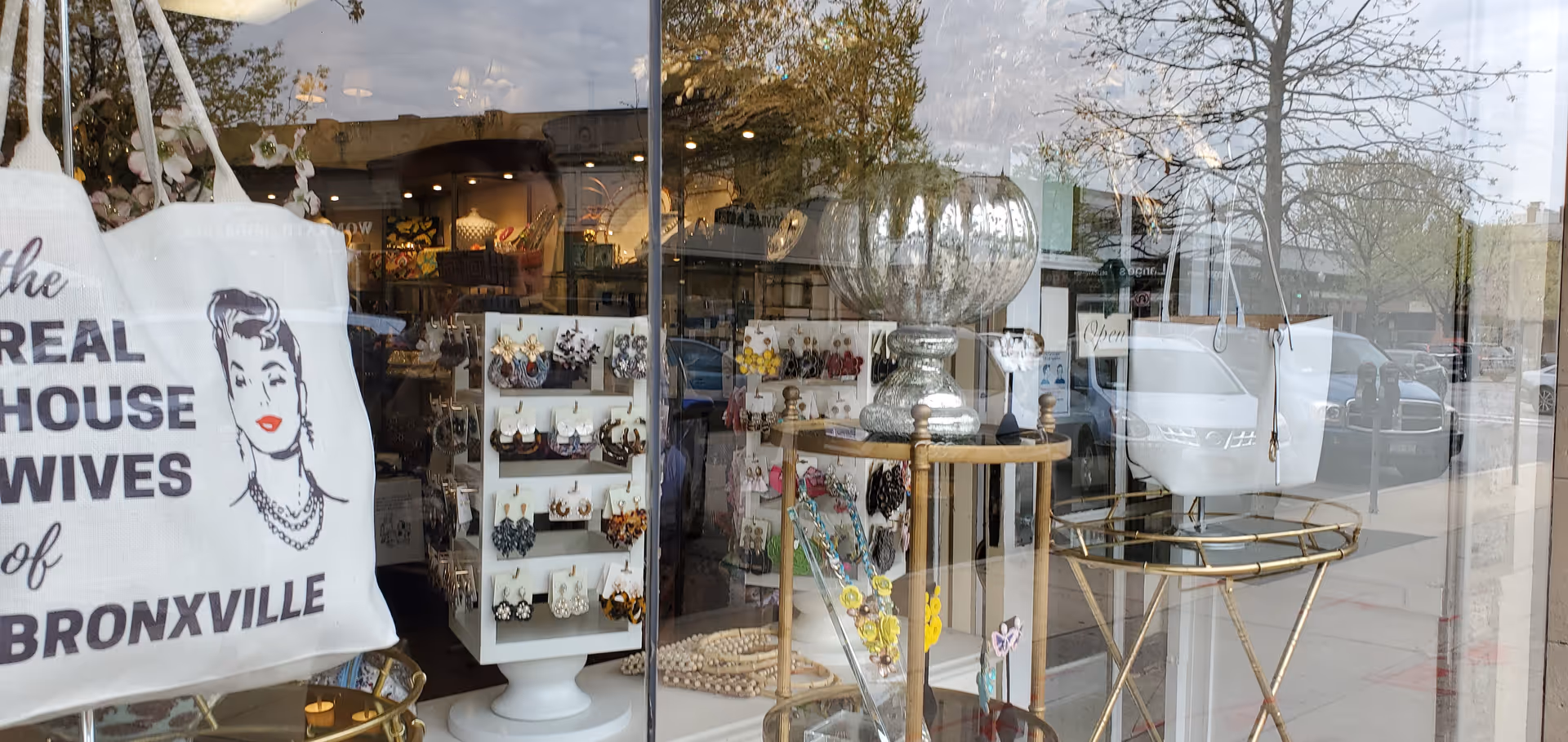 Storefront window display featuring jewelry and tote bags inside a boutique.