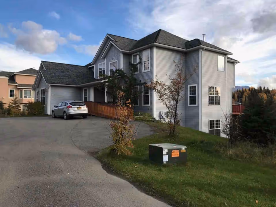 Two-story gray senior living building with a parking lot and small landscaped yard