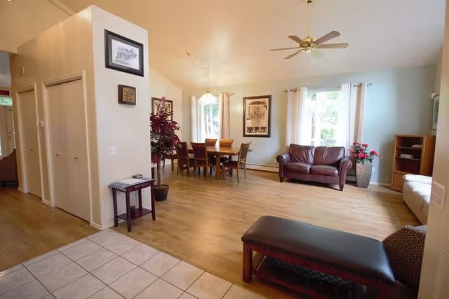 Spacious open living and dining area with hardwood floors, a dining table, a leather sofa, and large windows.