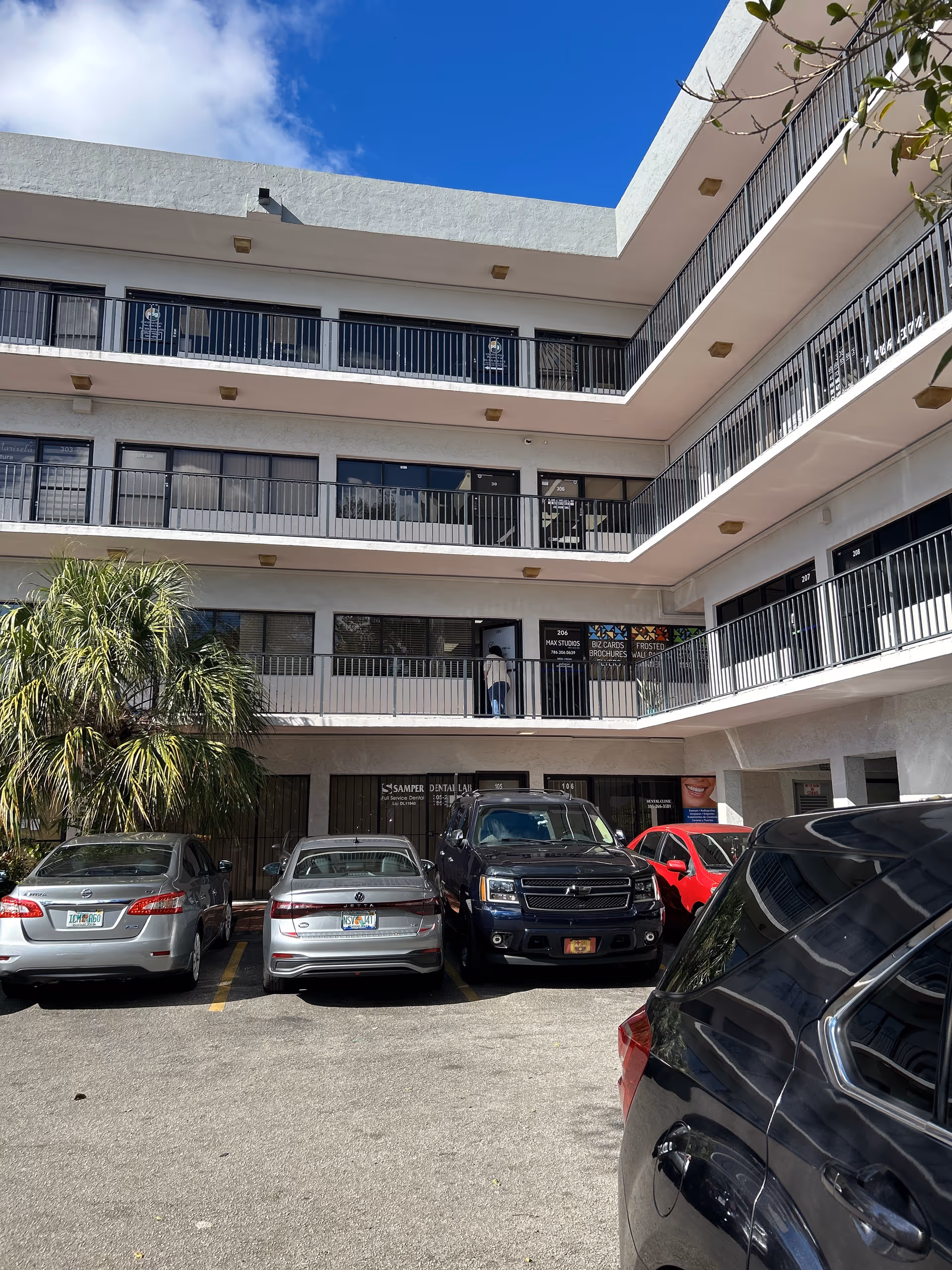 Three-story white senior living facility with balconies and a front parking lot.