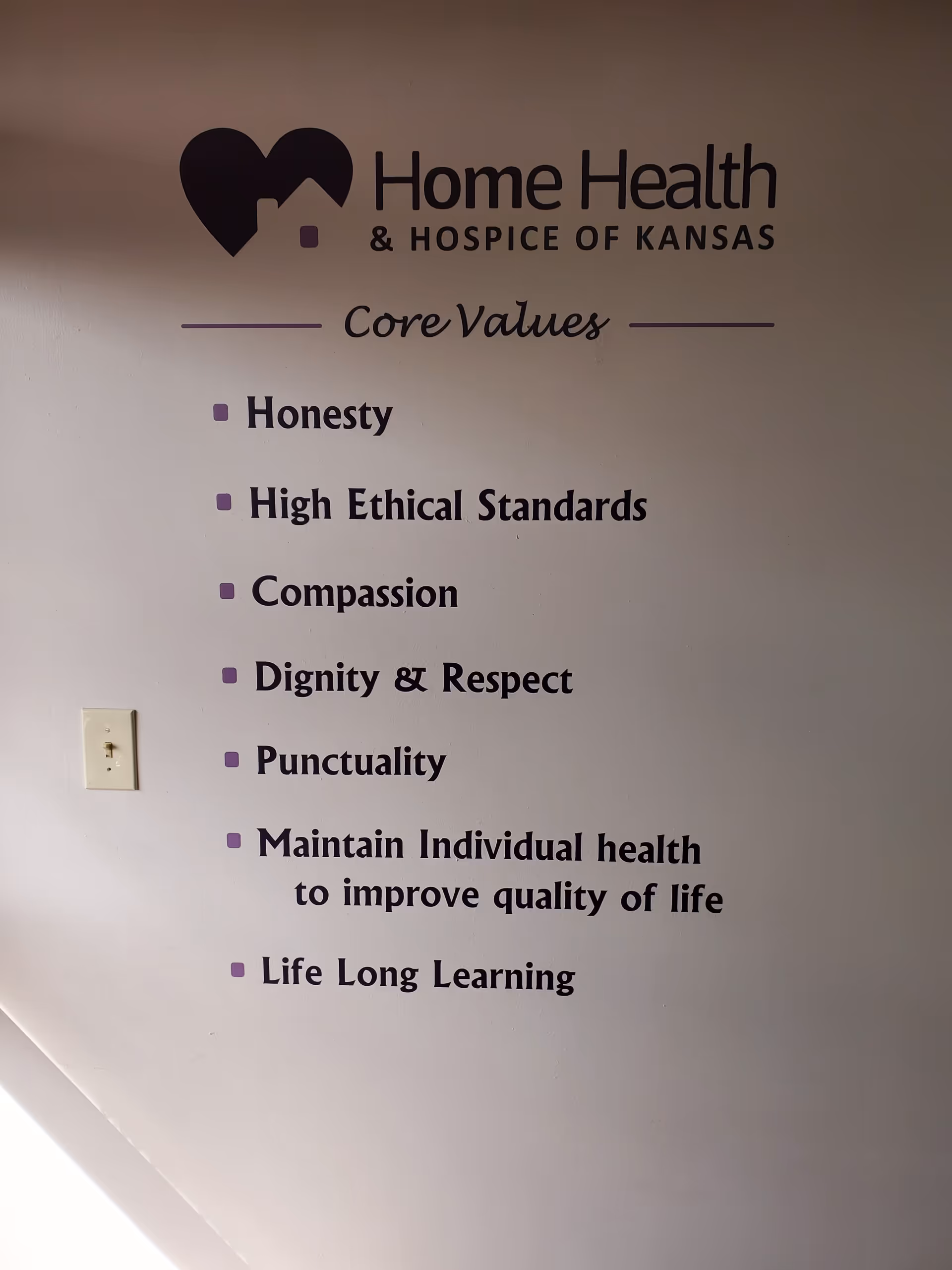 Interior wall displaying Home Health & Hospice of Kansas logo and core values list.