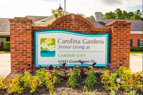 Brick entrance sign reading Carolina Gardens Senior Living at Garden City with landscaping.