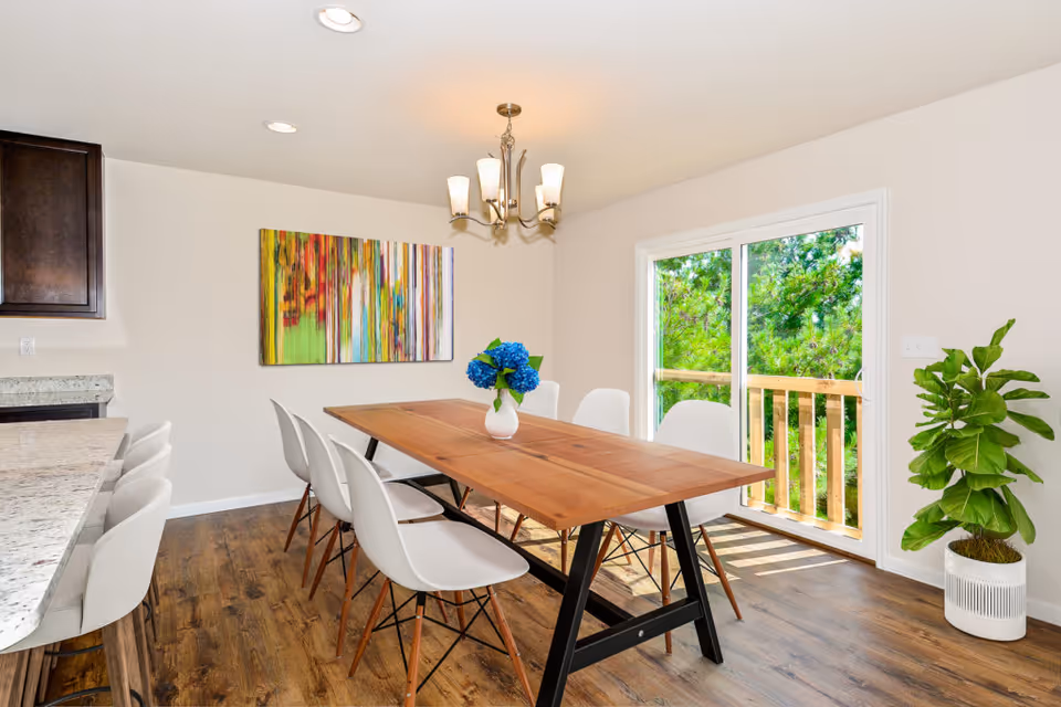 Bright dining room with a wooden table, white chairs, chandelier, and sliding glass door.