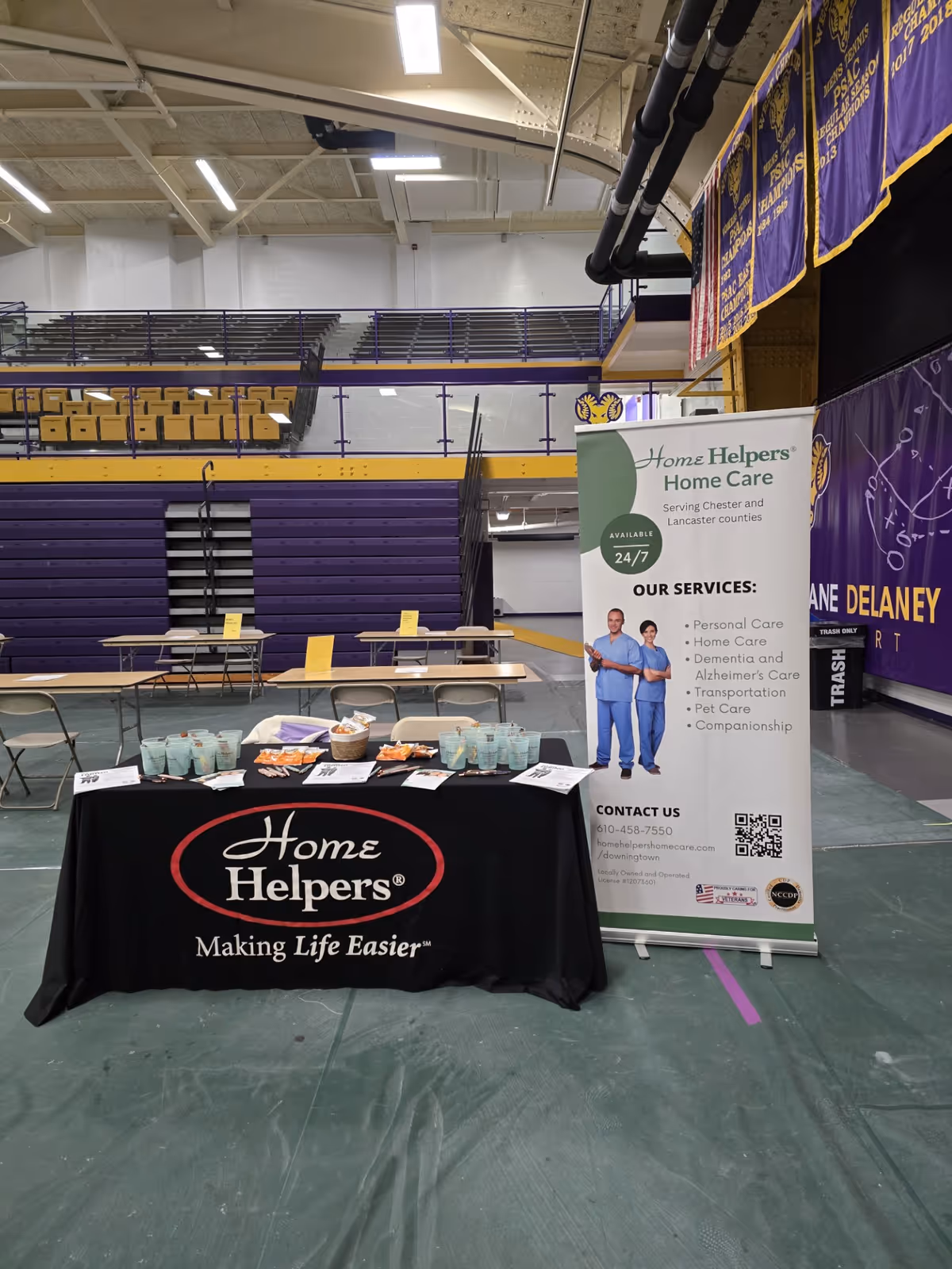 Indoor gym setup with a Home Helpers Home Care booth and banners.