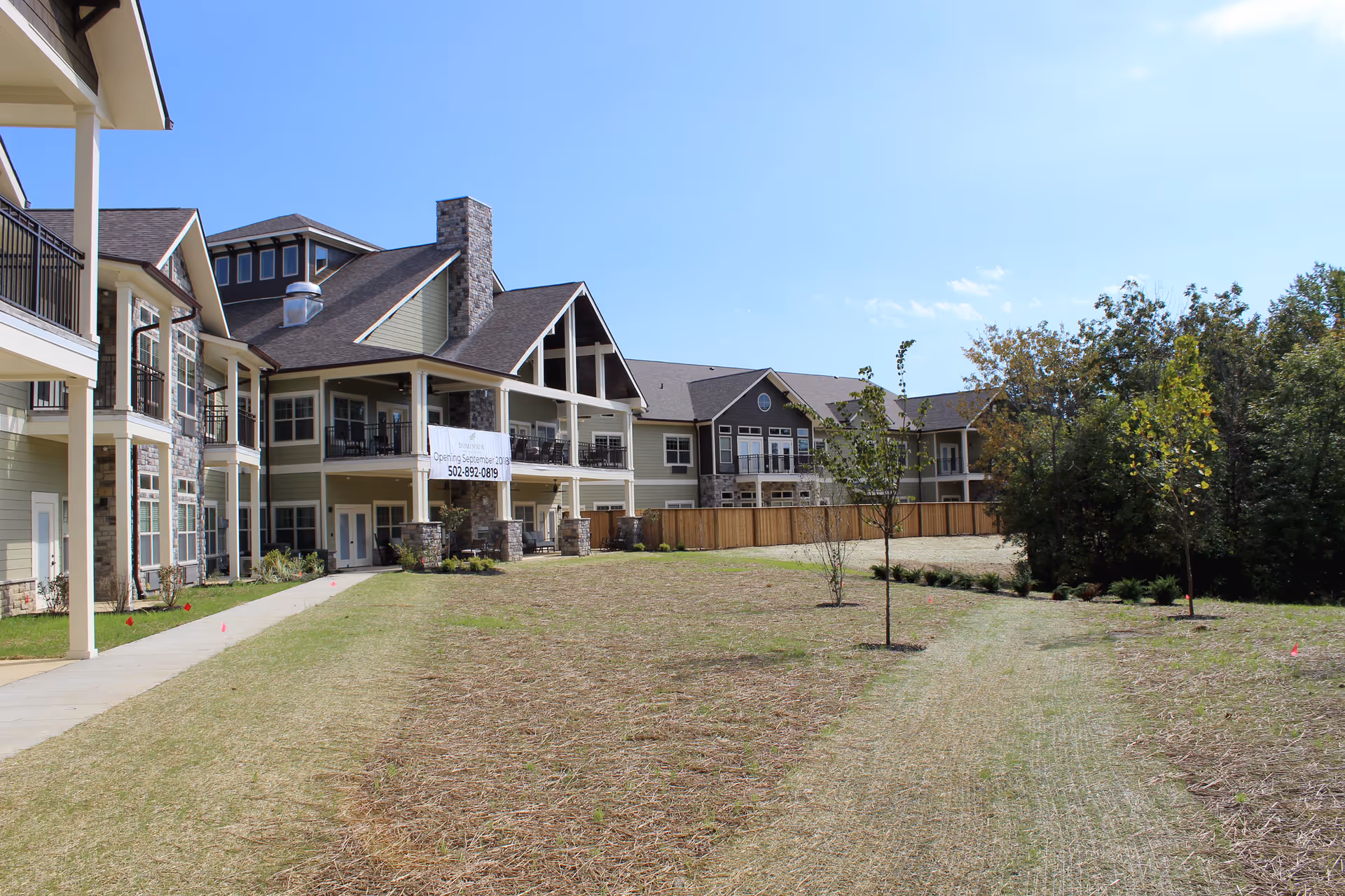 Exterior view of a multi-building senior living community with balconies and a grassy courtyard.