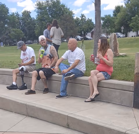 Several adults sit on a concrete bench at an outdoor park area.