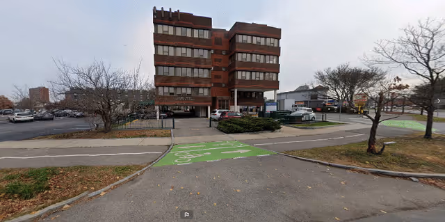 Exterior view of a brick building with parking and a green path