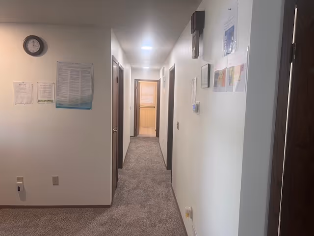 Long hallway inside a senior living facility with doors, posters, and a clock.