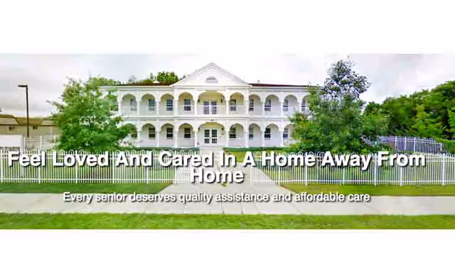 White, two-story senior living facility with arches, lawn, and a fence.