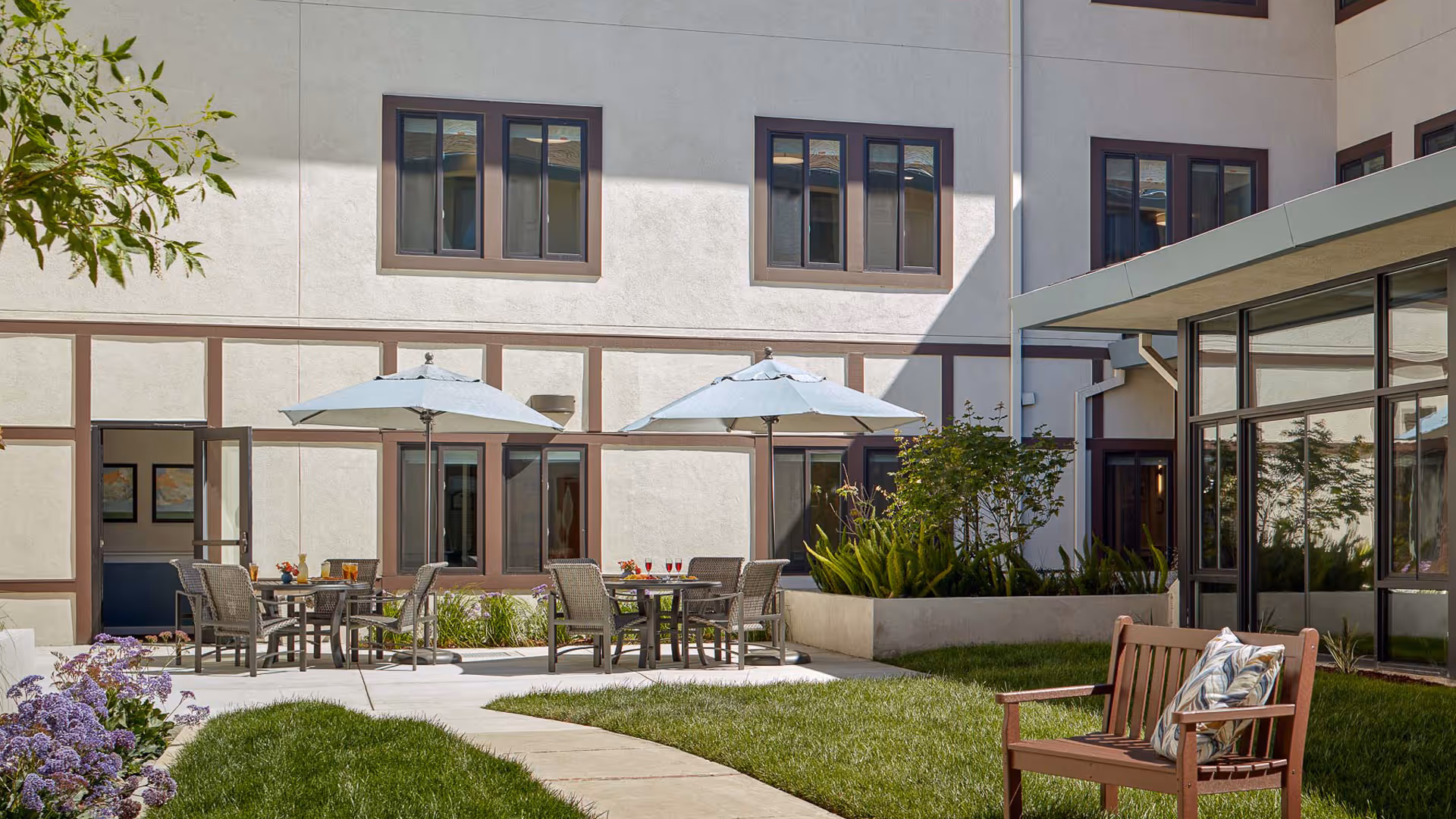 Courtyard outdoor seating area with tables, umbrellas, and a bench beside a modern building.