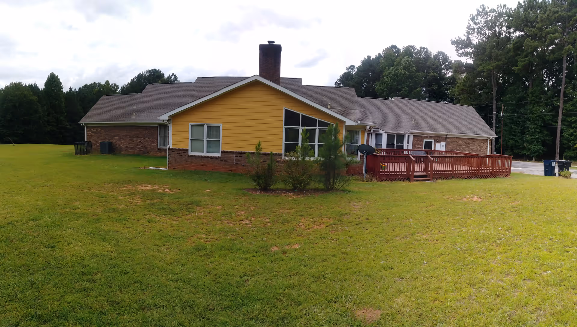 Single-story building with yellow siding, a wooden deck, and a large grassy yard.