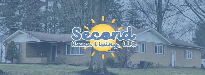 Single-story brick senior living facility with lawn, trees, and a logo reading Second Home Living, LLC