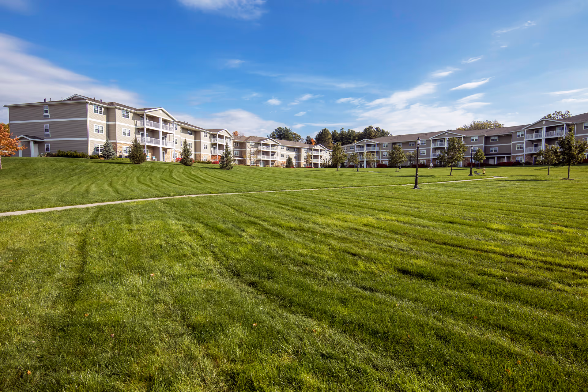 A wide manicured green lawn leading up to multiple low-rise apartment buildings under a blue sky.
