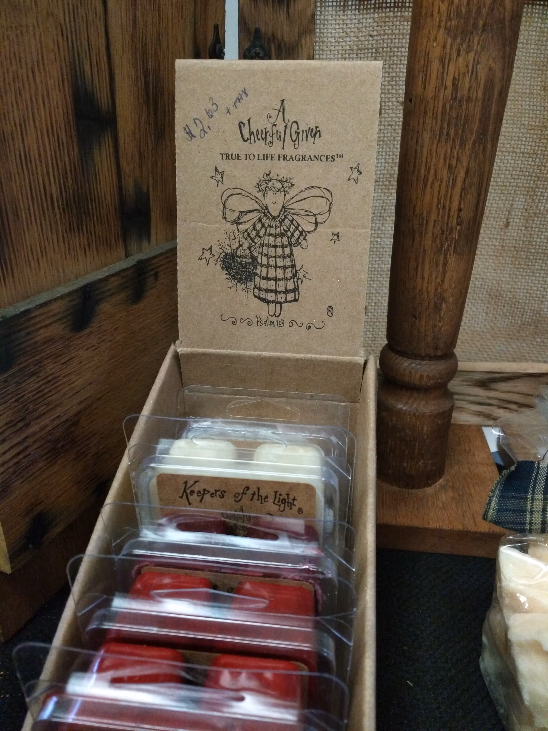 Open box displays A Cheerful Giver fragrance packaging and Keepers of the Light tins.