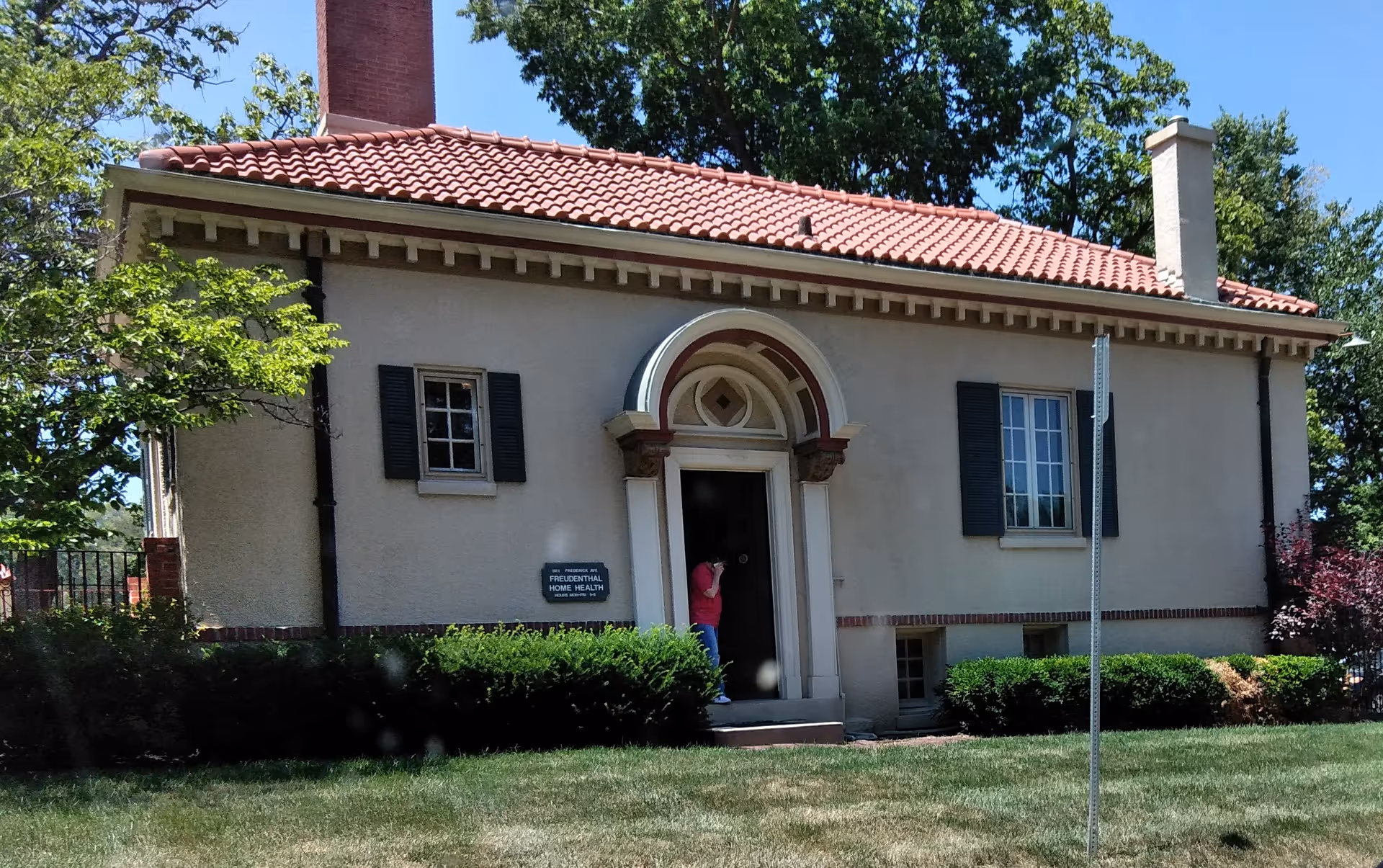 Small stucco building with red-tiled roof and arched doorway, Freudenthal Home Health sign