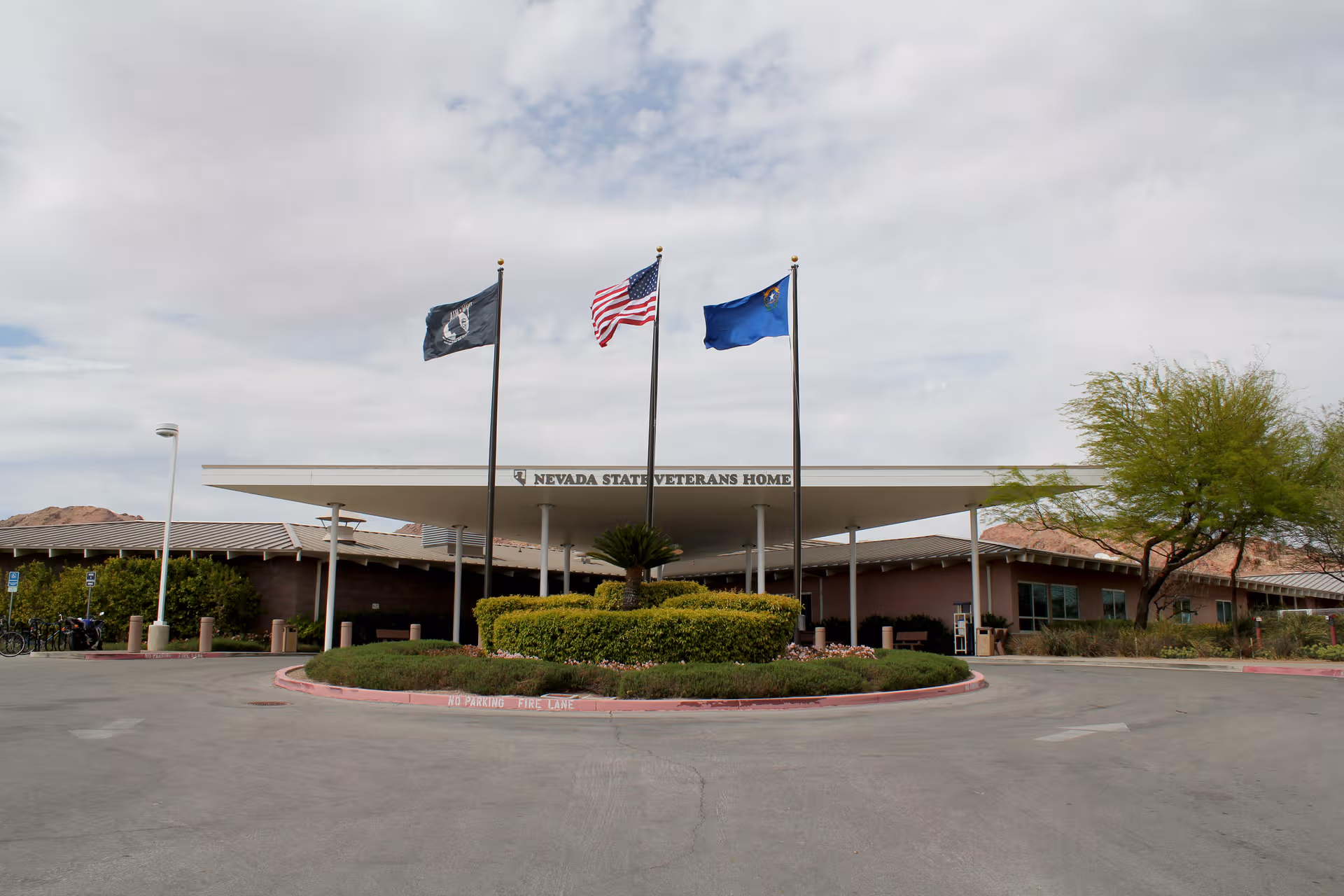 Front view of Nevada State Veterans Home entrance with flags and circular shrub bed.