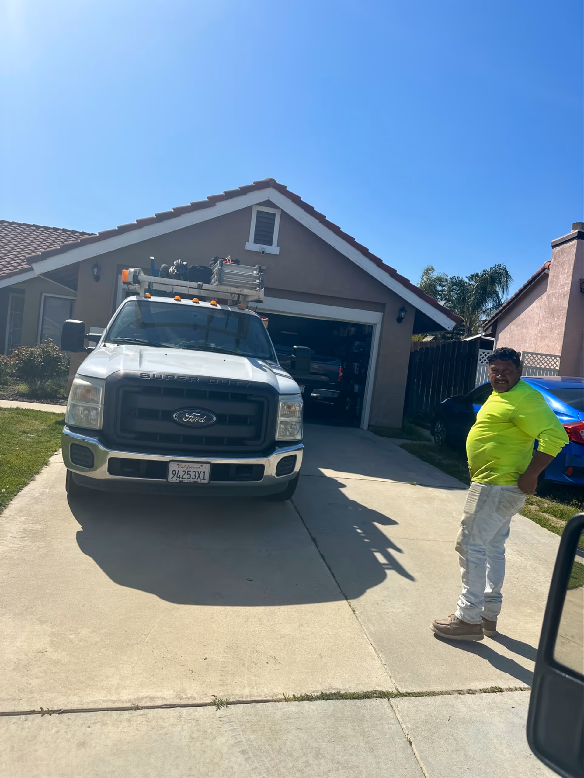 Front exterior of a house with a parked Ford truck and a man in neon shirt.