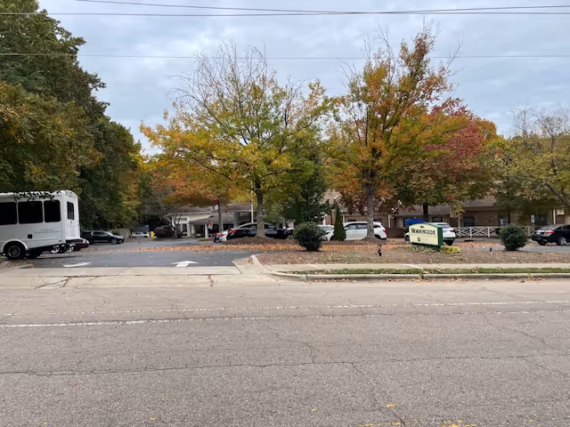 View of the exterior parking area and entrance of Morningside of Raleigh facility with several cars parked, trees with autumn foliage, and a sign displaying the facility's name.