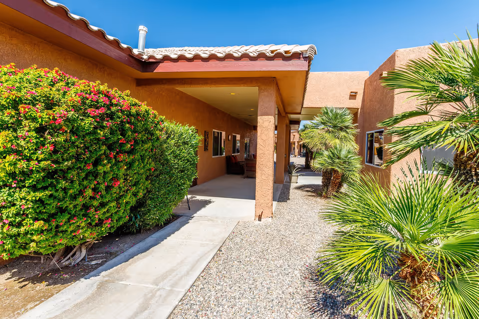 Desert landscaping surrounds a stucco assisted living building with a covered walkway.