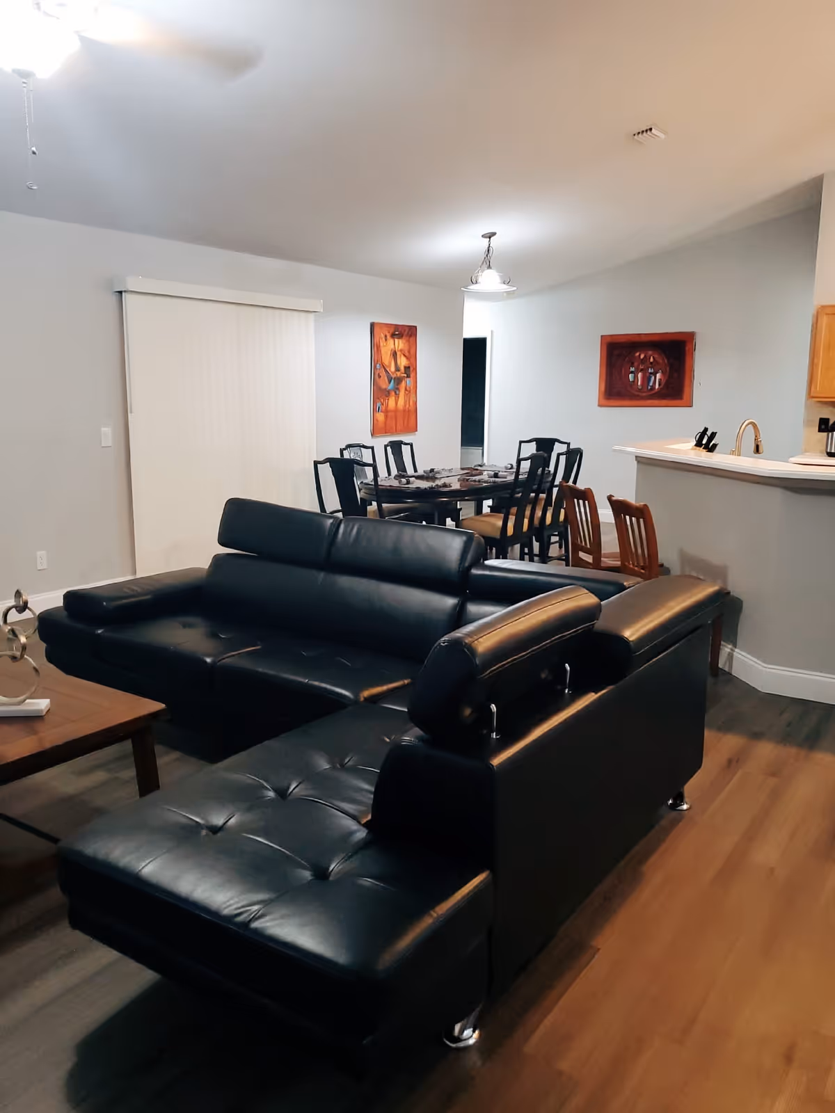 Open-concept living room with black leather sectional, dining area, and kitchen bar.