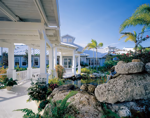 Exterior view of a light blue hospice building with a covered porch and tropical landscaping.