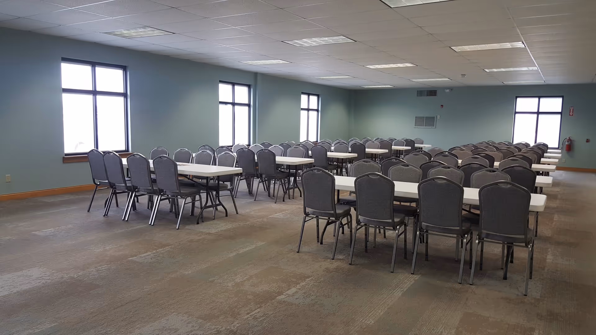 A large dining hall with rows of tables and gray chairs.