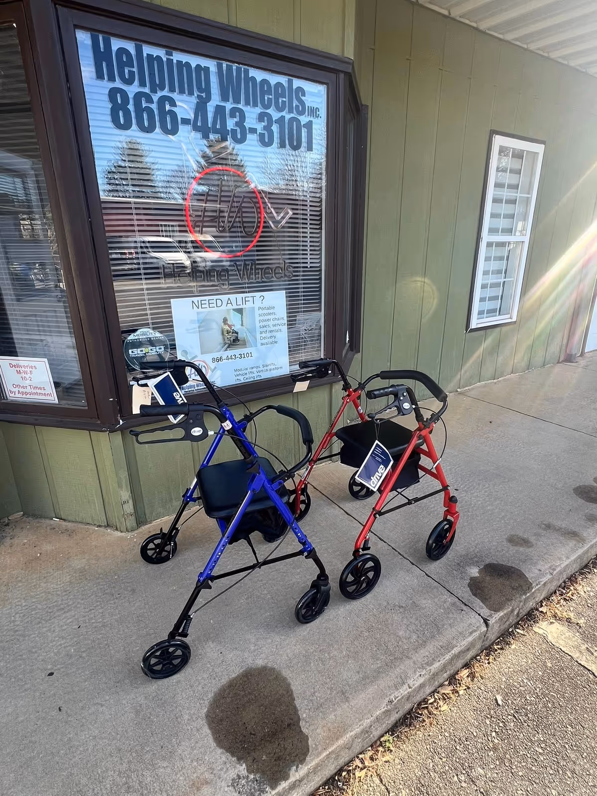 Two mobility scooters parked outside a green building with a large front window.