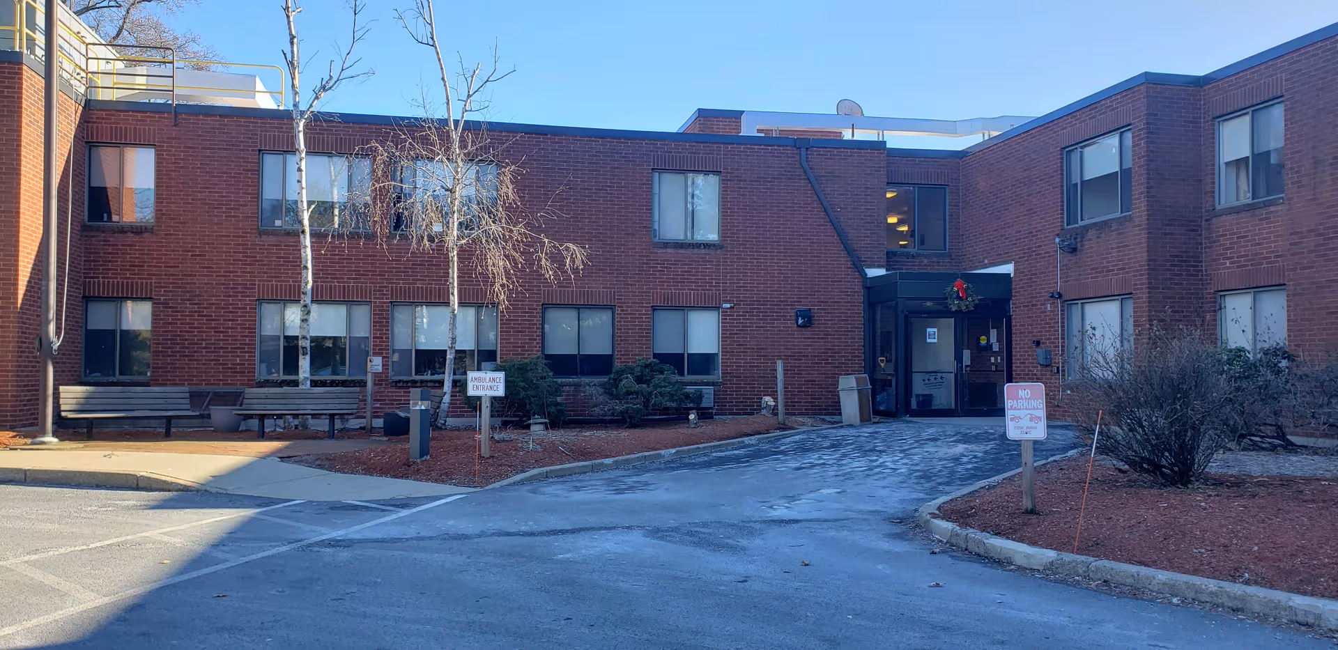 Brick senior living building with front entrance, benches, and landscaped surroundings.