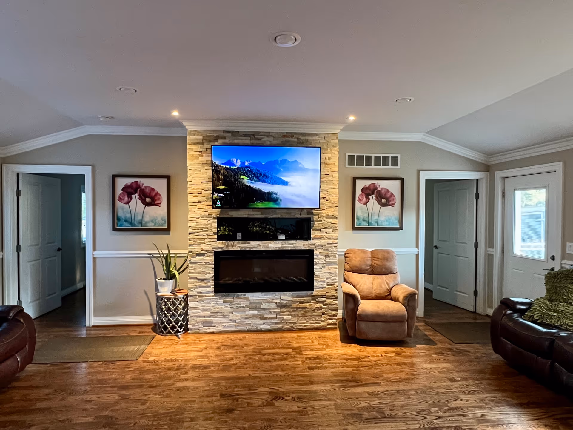 Cozy living room with stone fireplace, mounted TV, recliner, and framed artwork.