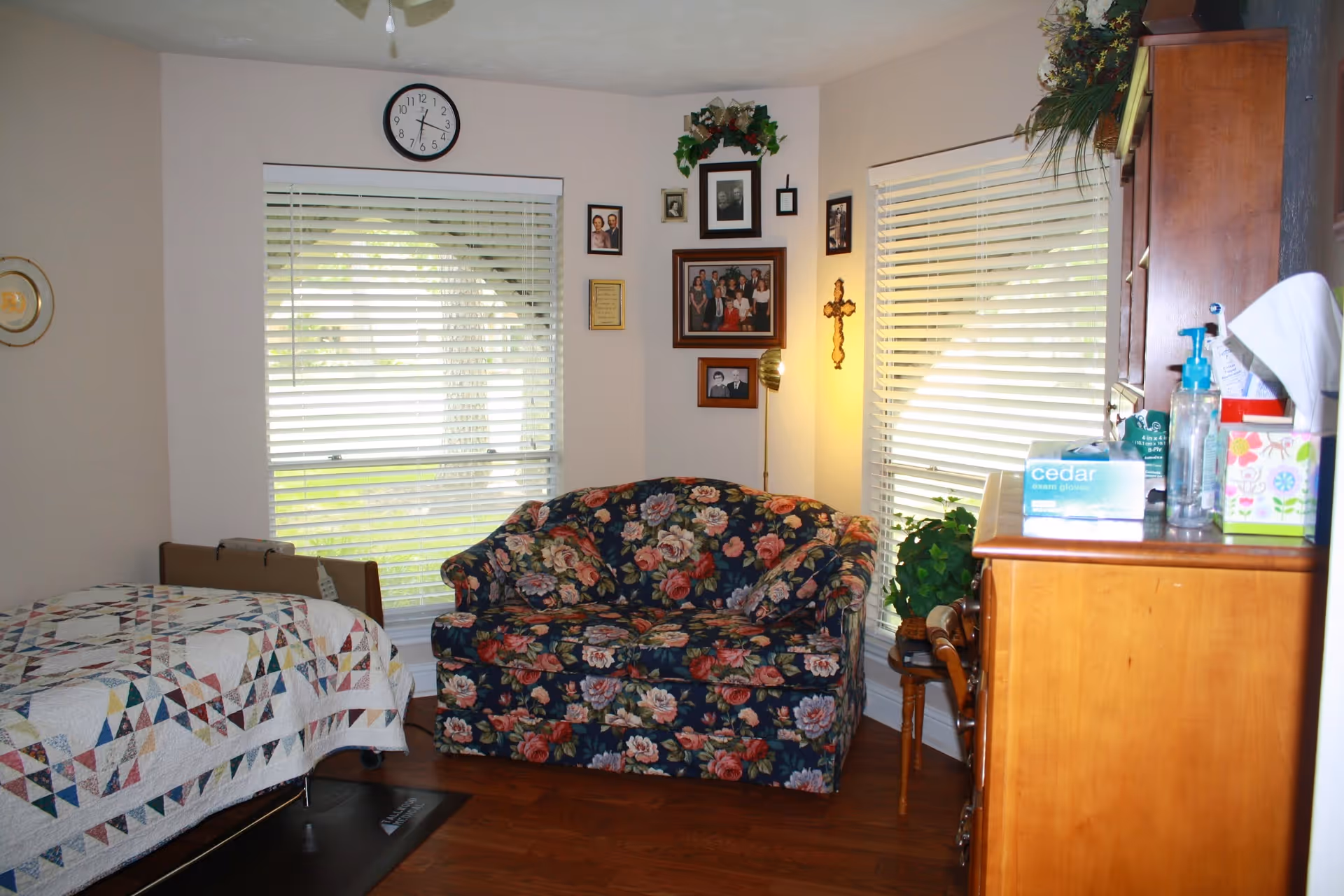 Cozy bedroom with a quilted bed, floral sofa, wall photos, and a dresser.