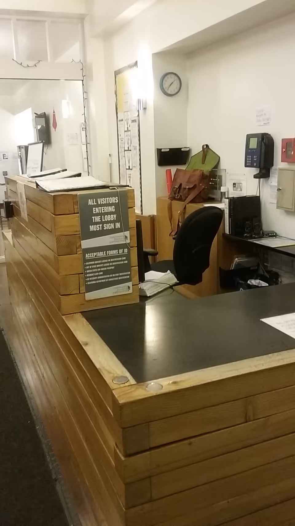 Wooden reception desk in a facility lobby with sign-in instructions and office equipment.
