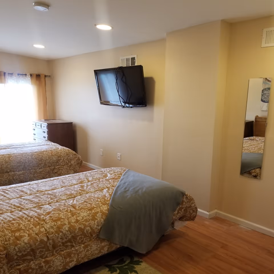 Two single beds with patterned quilts, dresser, mounted TV in a softly lit bedroom.