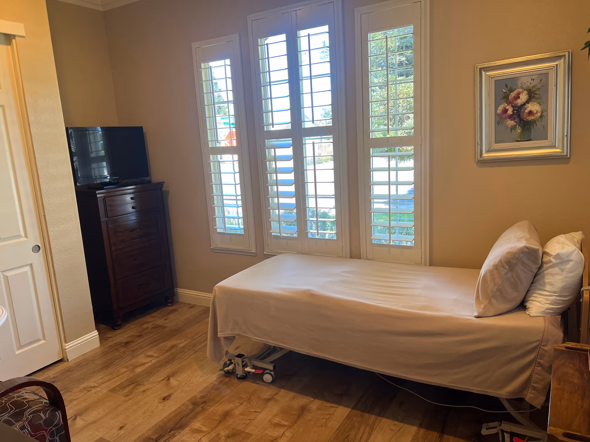 Bedroom with a bed, dresser, TV, and tall windows with shutters.