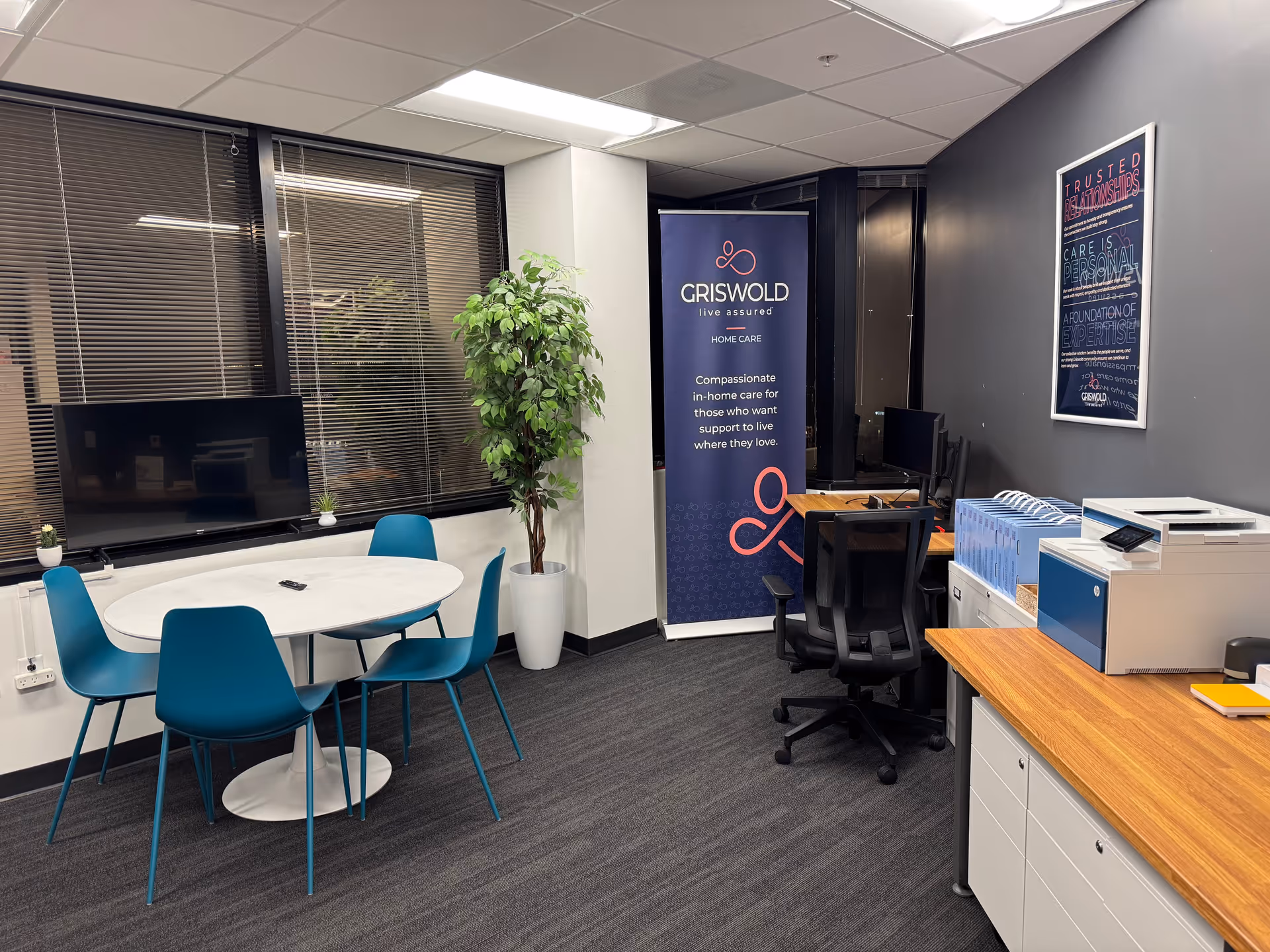 Interior office area with Griswold banner, round table, blue chairs, and office equipment.