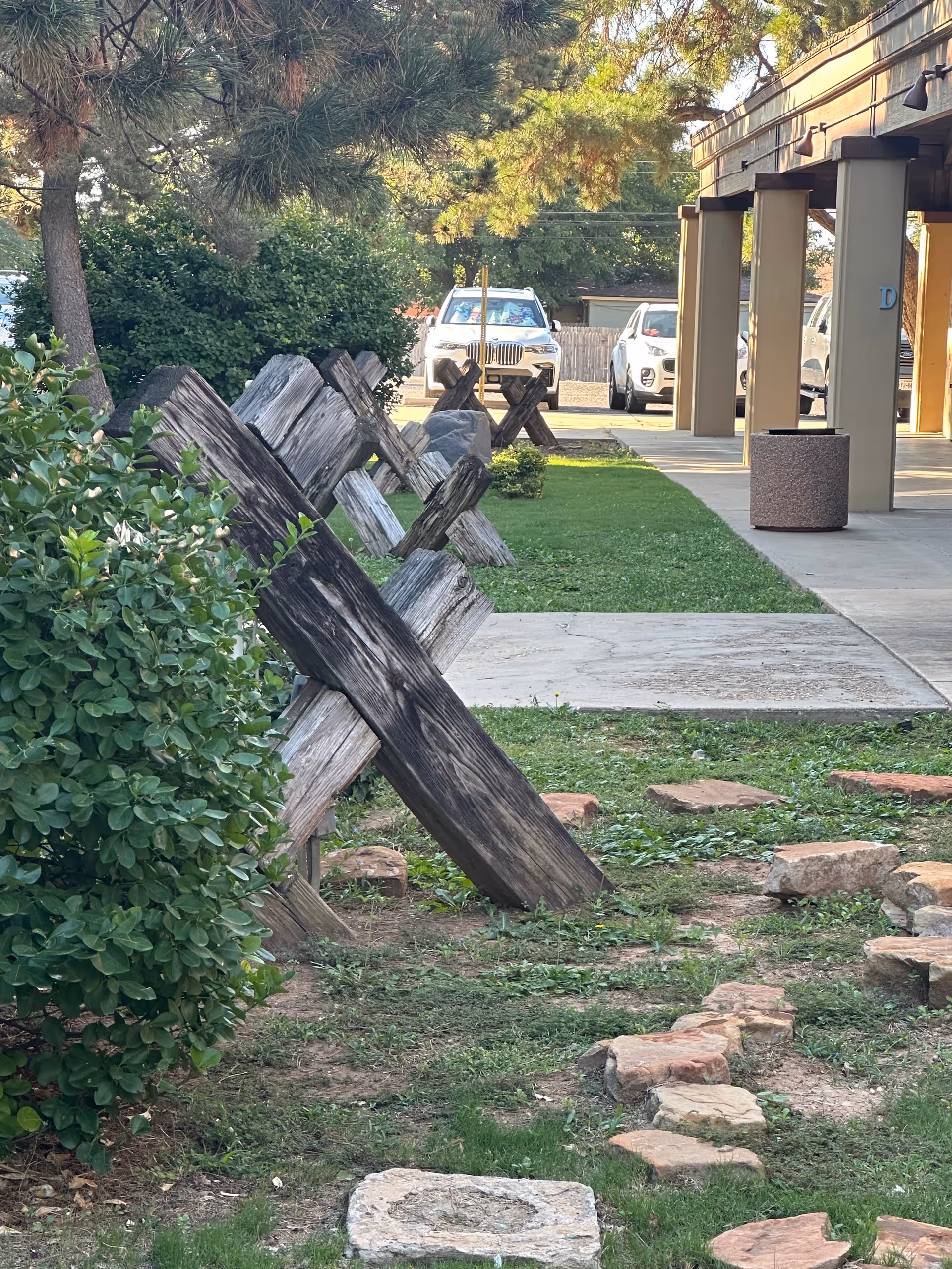 Outdoor view of a senior care facility with a leaning wooden fence, greenery, and parked cars.