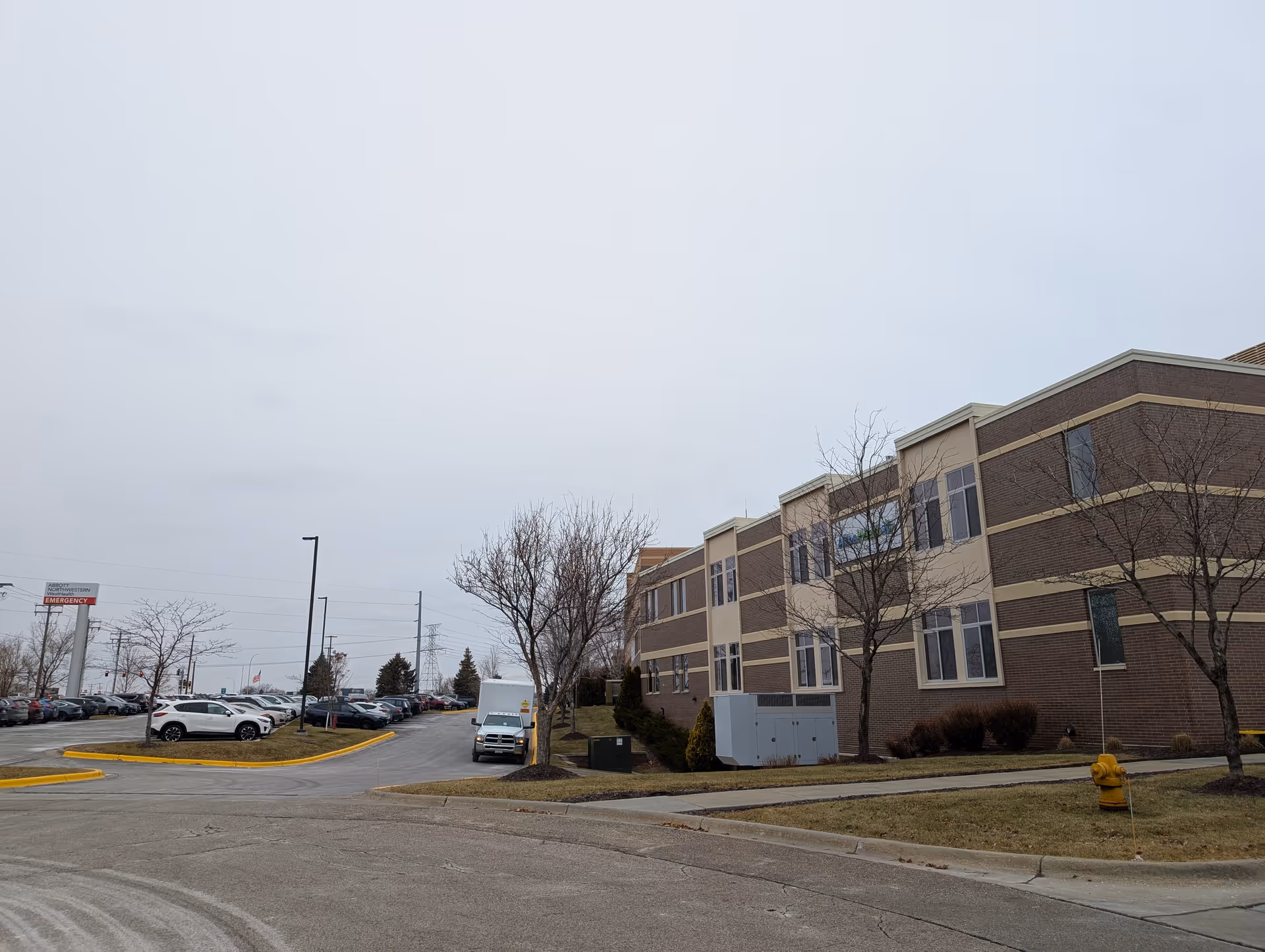 Exterior view of a two-story brick senior living building with a parking lot, bare trees, and an overcast sky.