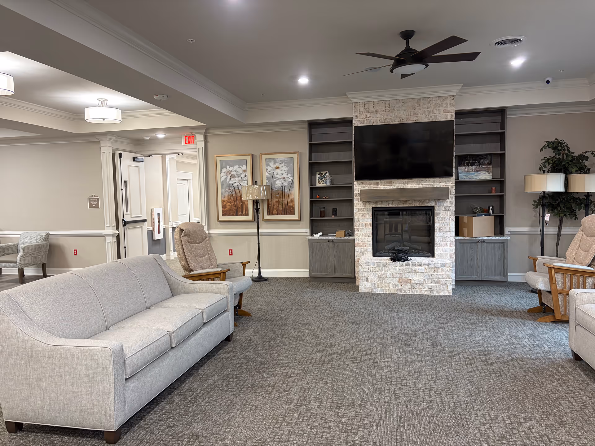 Spacious senior living lounge with sofa, chairs, fireplace, and mounted TV.