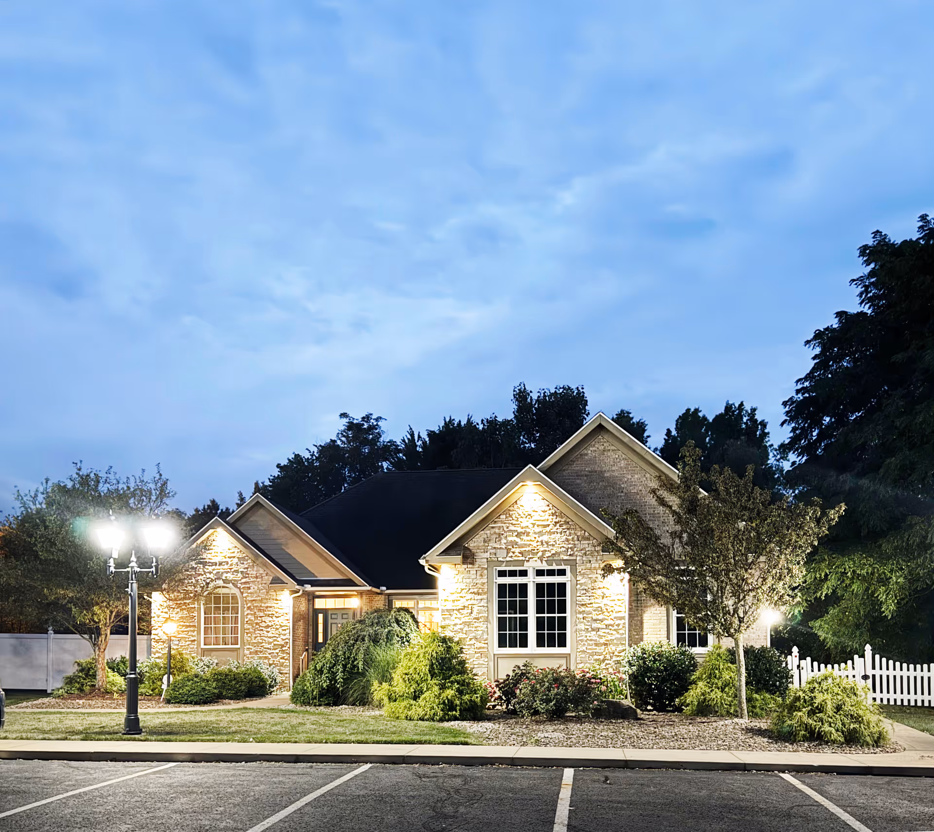 Front view of a stone hospice building with landscaped yard at dusk.