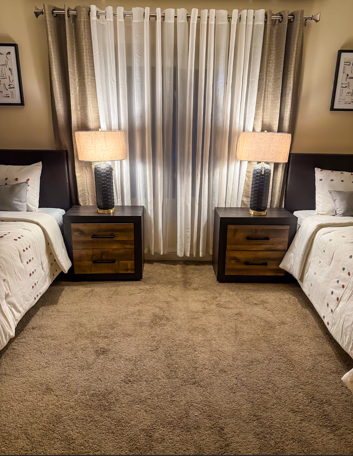 Twin beds with matching nightstands and lamps flank a window with sheer curtains.
