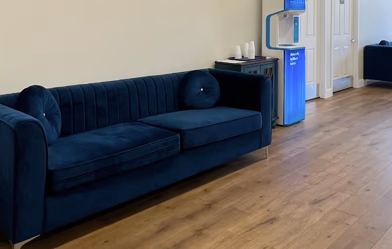 Blue velvet sofa in a bright senior living lounge with wood floors and a water cooler.
