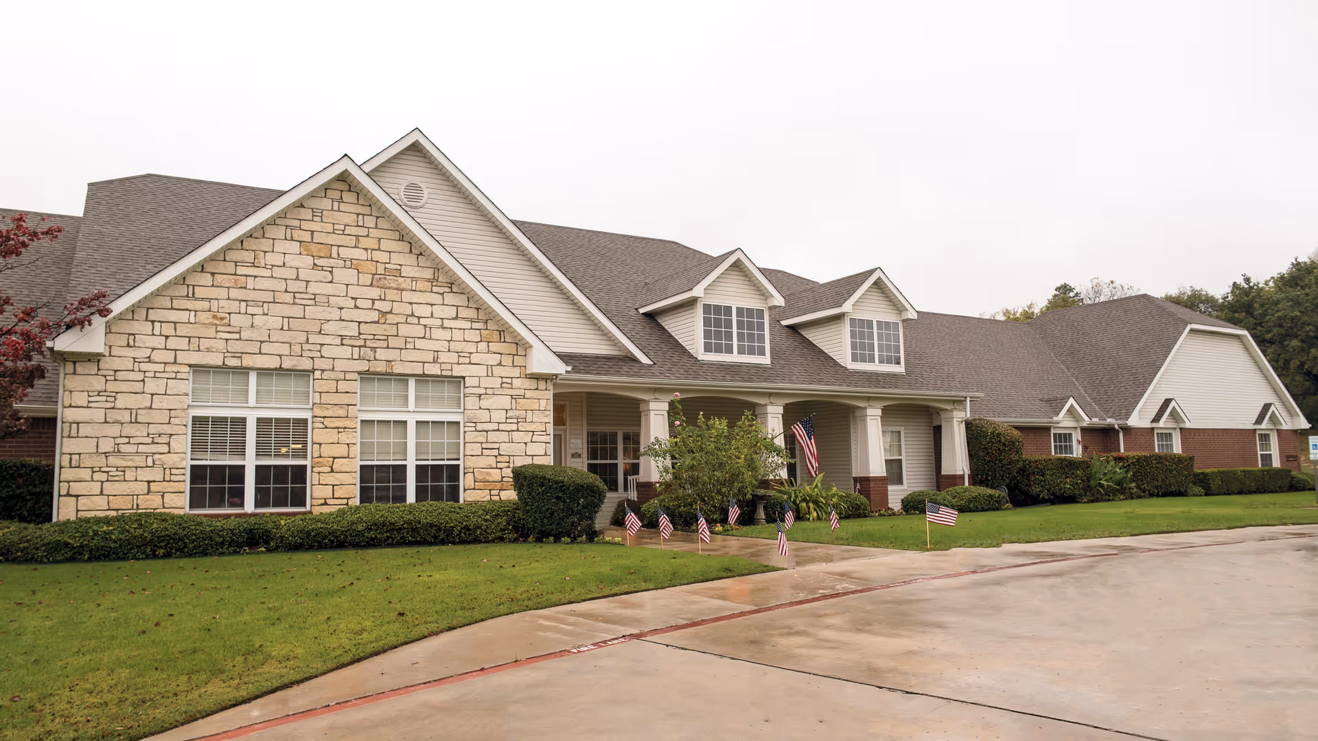 Exterior view of Oxford Springs Weatherford showing stone facade, manicured lawn, and flag-lined entrance.