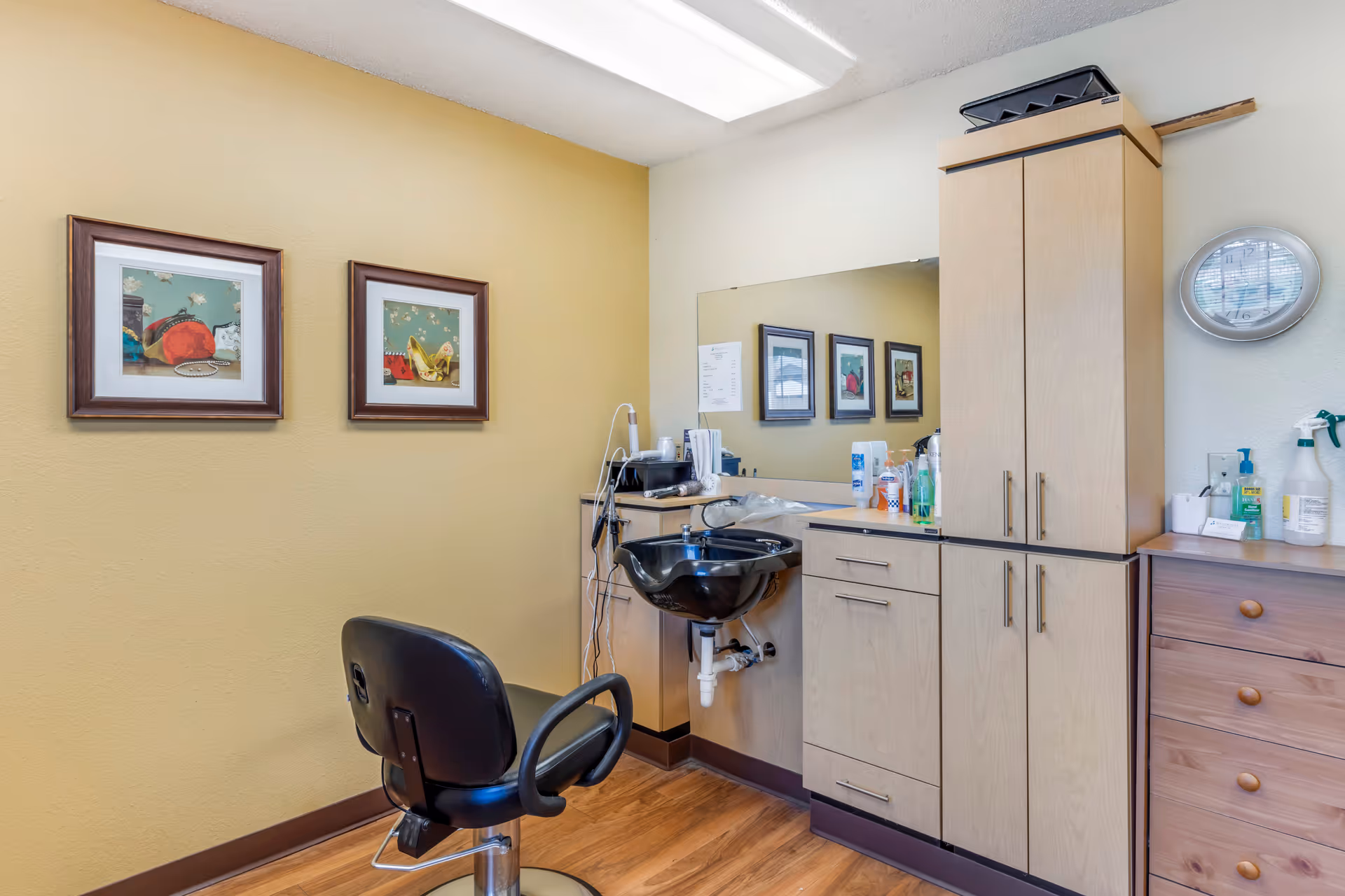 Hair salon station with sink, chair, cabinets, mirror, and framed art in a warm interior.