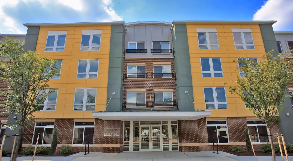Front view of Victory Square Apartments building with colorful panels and glass entry.