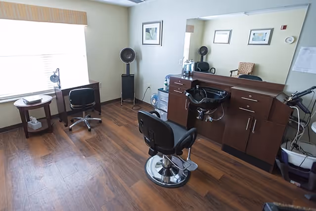 Interior salon room with styling chairs, a shampoo sink and cabinets in front of a large mirror and wood floors.